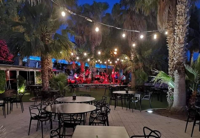 Il dehors di CLORO di sera: palme, luci a filo calde e palco per la musica dal vivo a bordo piscina